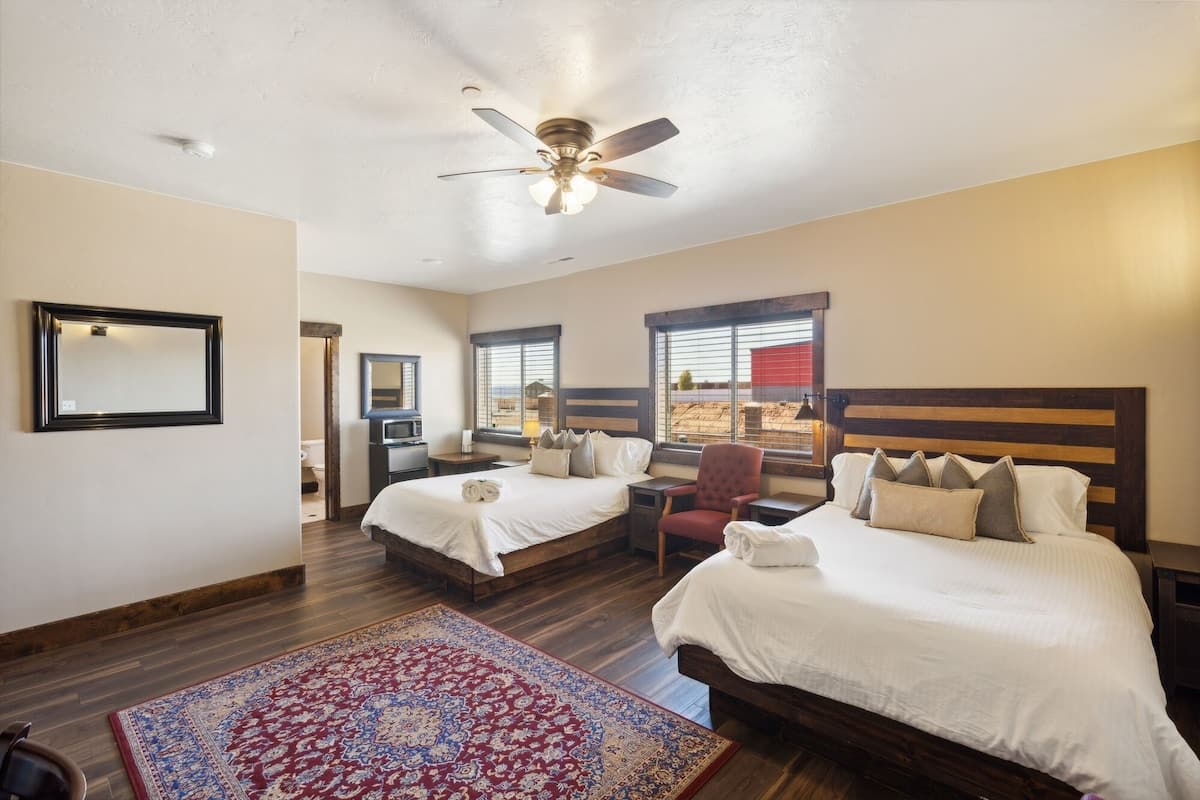 A hotel room with two beds, a ceiling fan, a large window, and a view of the desert.