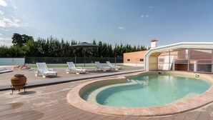 Una piscina con sillones de descanso, una pérgola y un edificio moderno al fondo.