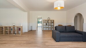 Un salón amplio con un sofá gris, estanterías de madera y una lámpara colgante.