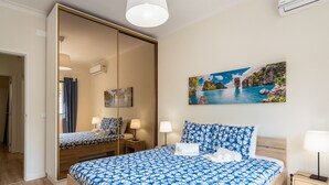 Habitación de hotel con una cama grande, un espejo, un cuadro y una mesita de noche con lámpara.
