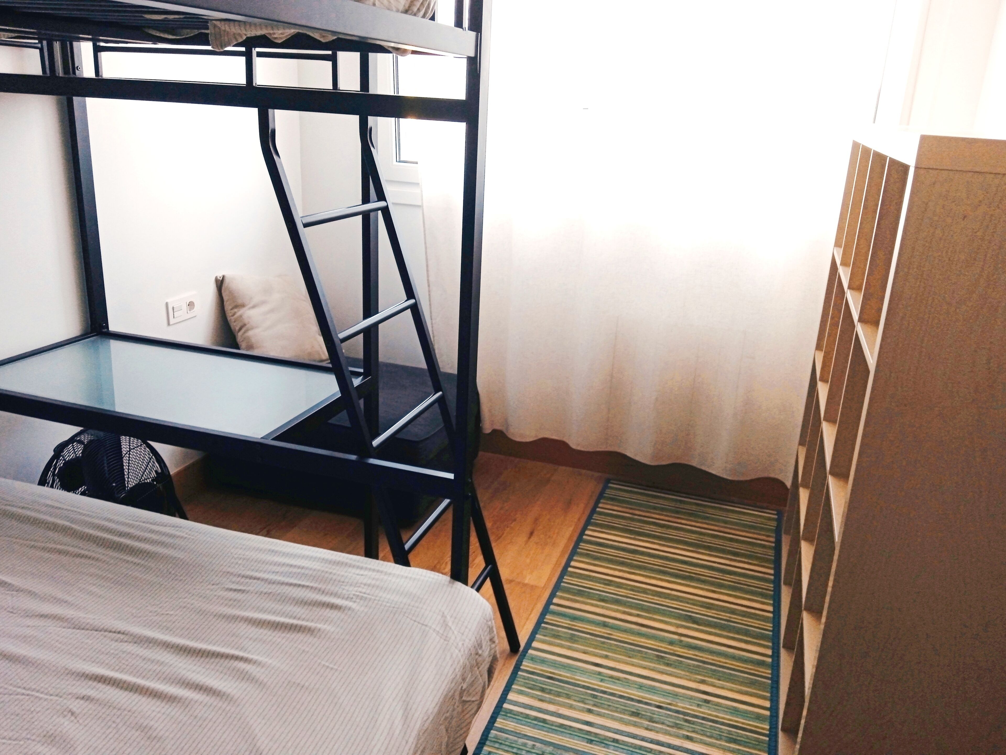 Un lit superposé avec un bureau et une chaise, un petit tapis et un coussin sur le sol.