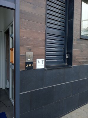Een gevel van een gebouw met houten lambrisering, een metalen luik en een bord met de tekst '2B PB 11'.