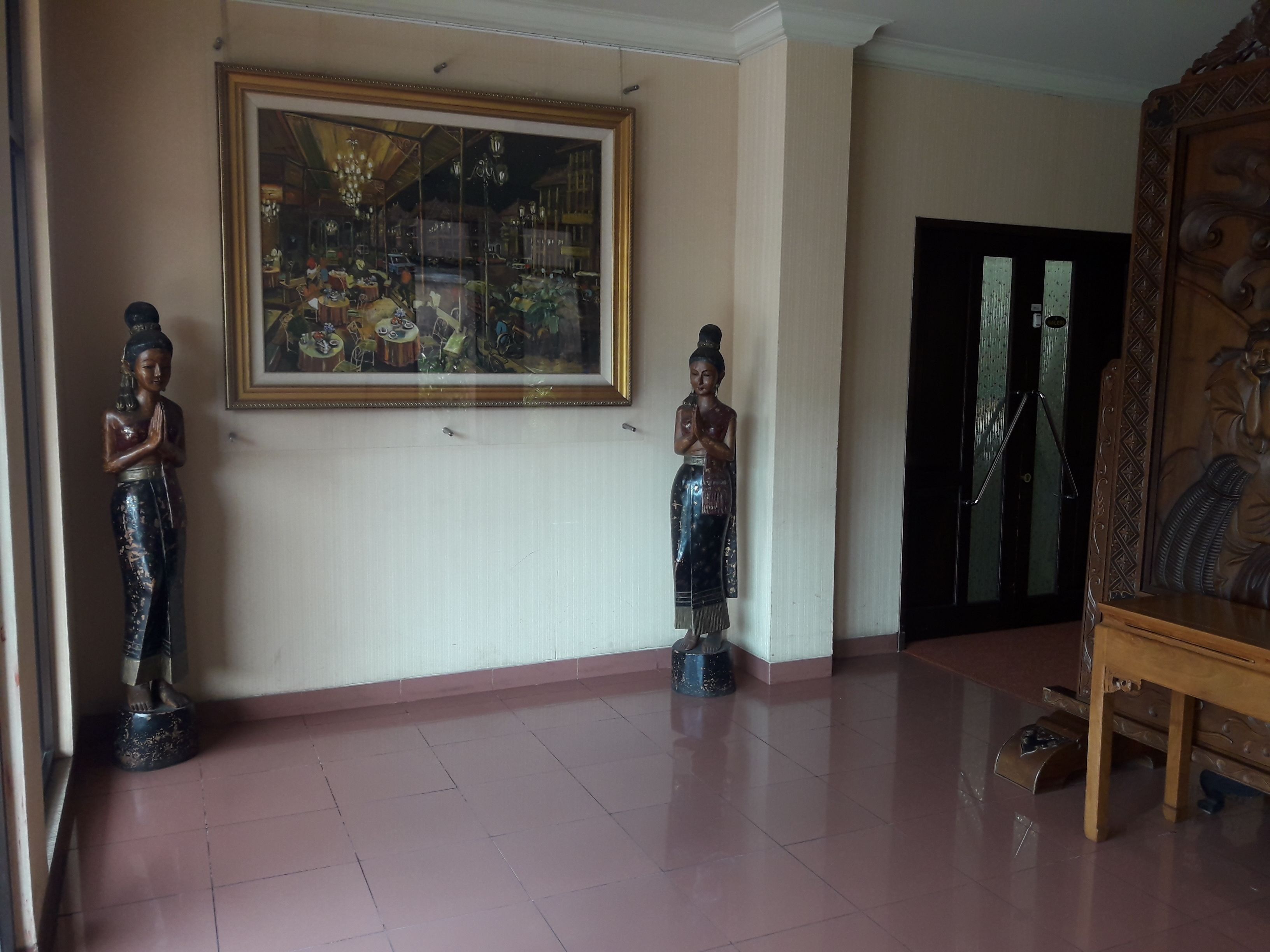 A room with a large framed painting on the wall, two statues, a wooden cabinet, and a door with a mirror.