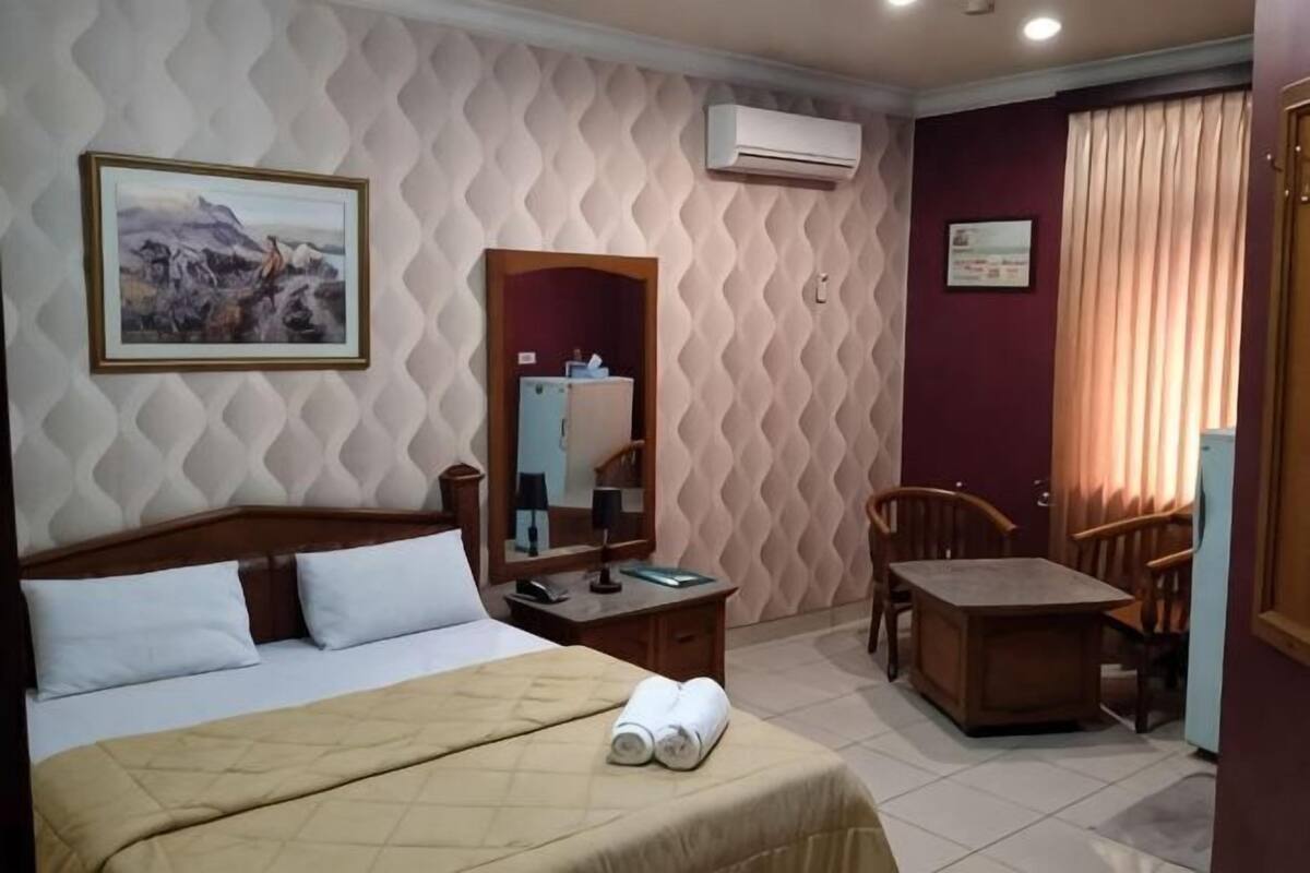 A hotel room with a bed, a desk, a chair, a mirror, and a window with curtains.