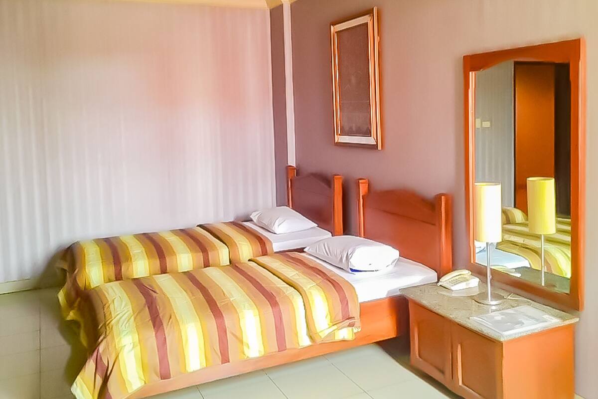 A hotel room with a bed, a bedside table with a lamp, a telephone, and a mirror.