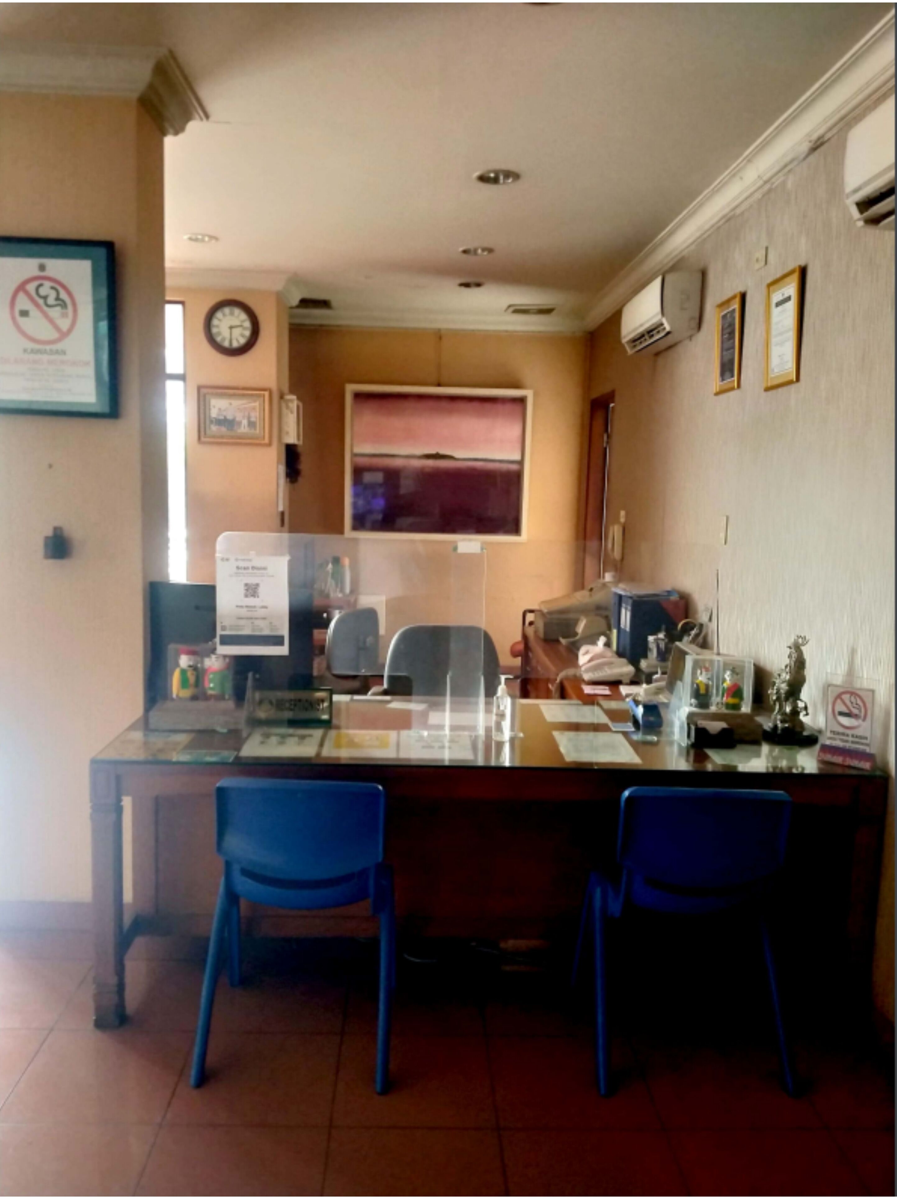 A conference room with a glass table, two blue chairs, a clock, and a window with a view.