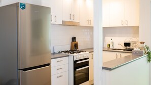 A modern kitchen with white cabinets, a stainless steel refrigerator, a gas stove, and an oven. - Lotus Stay Manly - Apartment 31F (Manly)