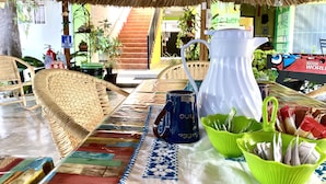 A room with a thatched roof, wicker furniture, a patterned tablecloth, and a variety of items including a white pitcher, a blue mug, and a green bowl. - Hostal Casa Huasteca (Ciudad Valles)