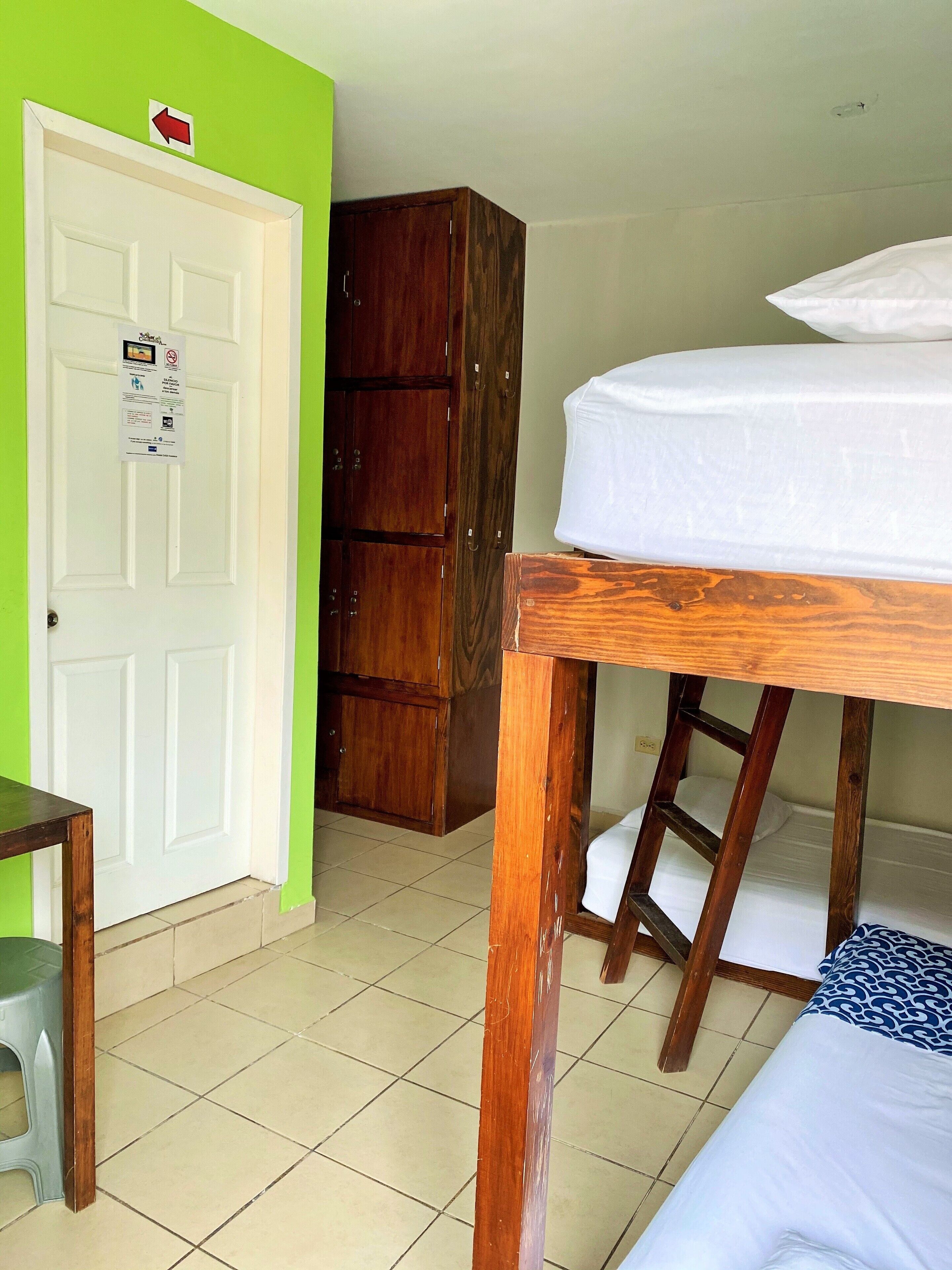 Una habitación con una cama litera, un armario de madera, un escritorio con silla y una puerta con un cartel.