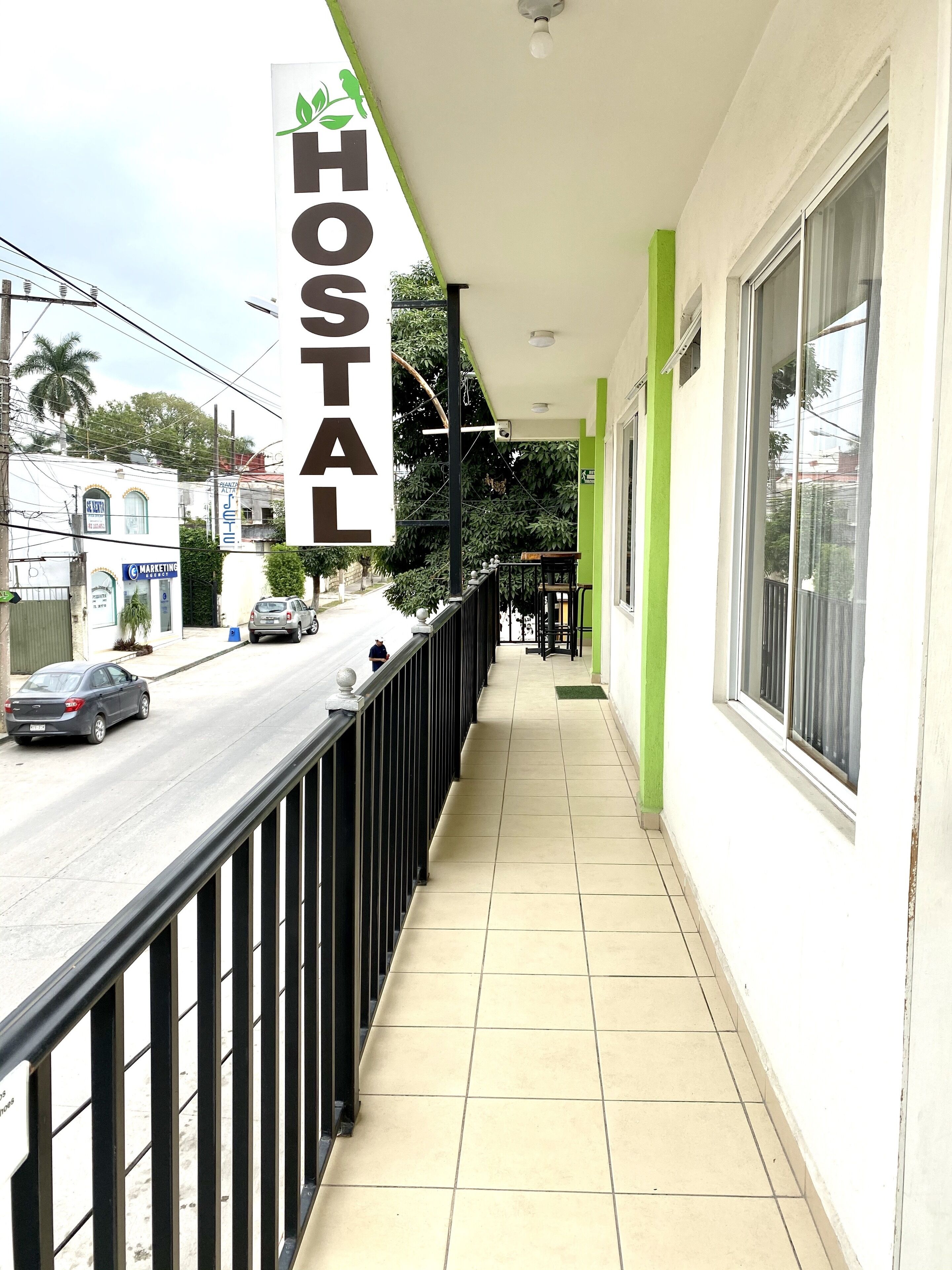 A hotel corridor with a sign reading "HOSTAL" and a view of the street with cars and buildings.