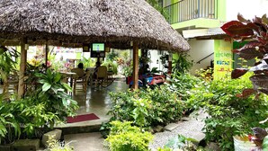 A thatched-roof outdoor seating area with tables and chairs, surrounded by lush greenery and potted plants. - Hostal Casa Huasteca (Ciudad Valles)