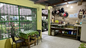 A dining area with a table and chairs, a kitchen with pots and utensils, and a view through a window. - Hostal Casa Huasteca (Ciudad Valles)