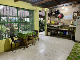 A dining area with a table and chairs, a kitchen with pots and utensils, and a view through a window.