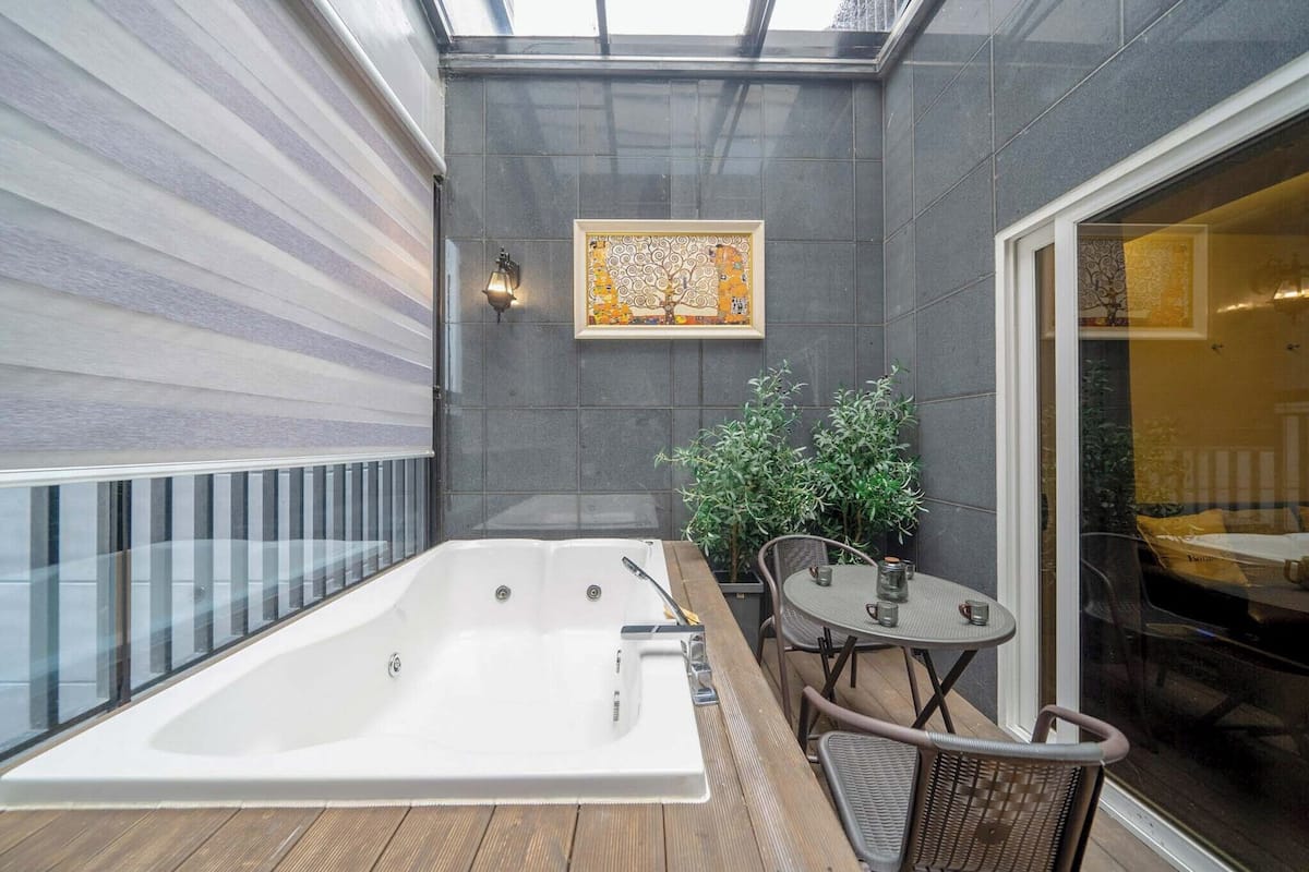 A spa area with a large bathtub, a small table with chairs, and a potted plant.