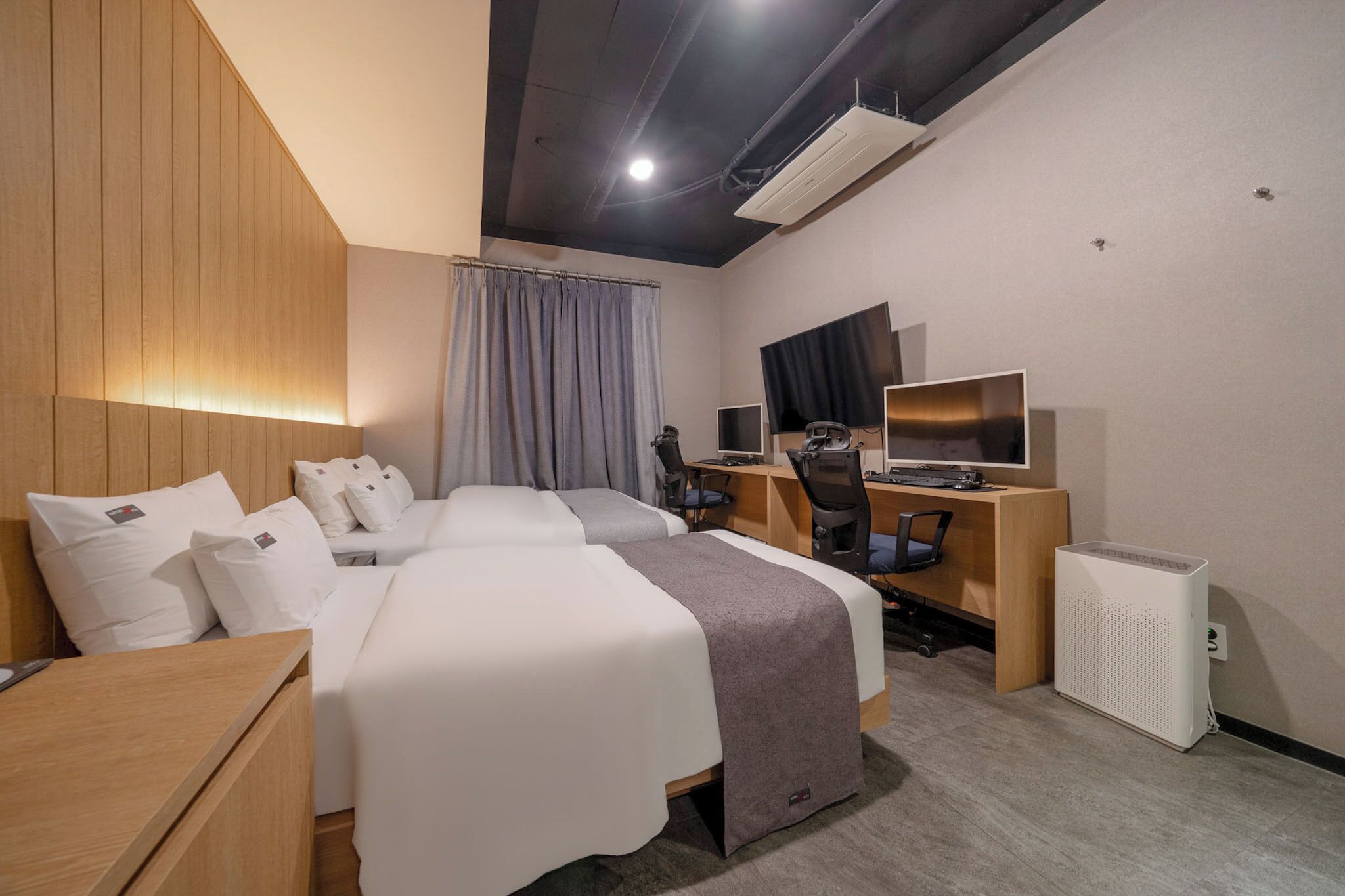 Une chambre d’hôtel avec deux lits, un bureau, une chaise, une télévision et un appareil de climatisation.
