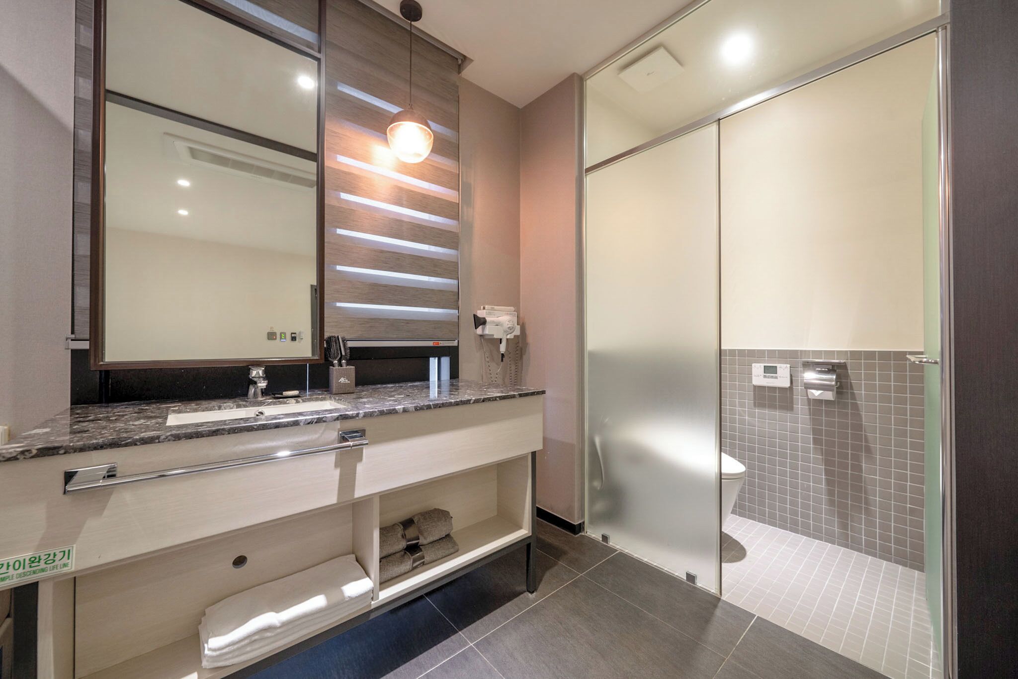 A modern bathroom with a large mirror, a marble countertop, a towel rack, and a glass shower enclosure.