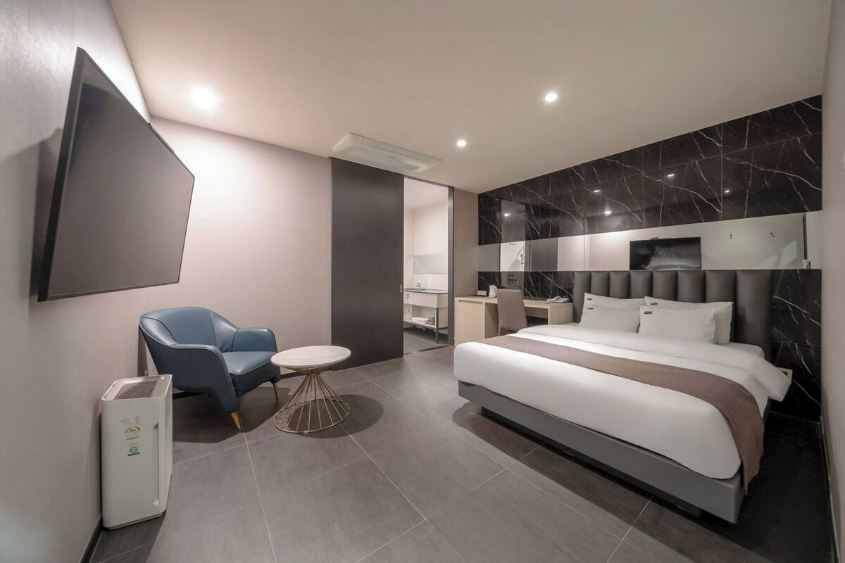 A modern hotel room with a bed, a desk, a chair, and a TV mounted on the wall.