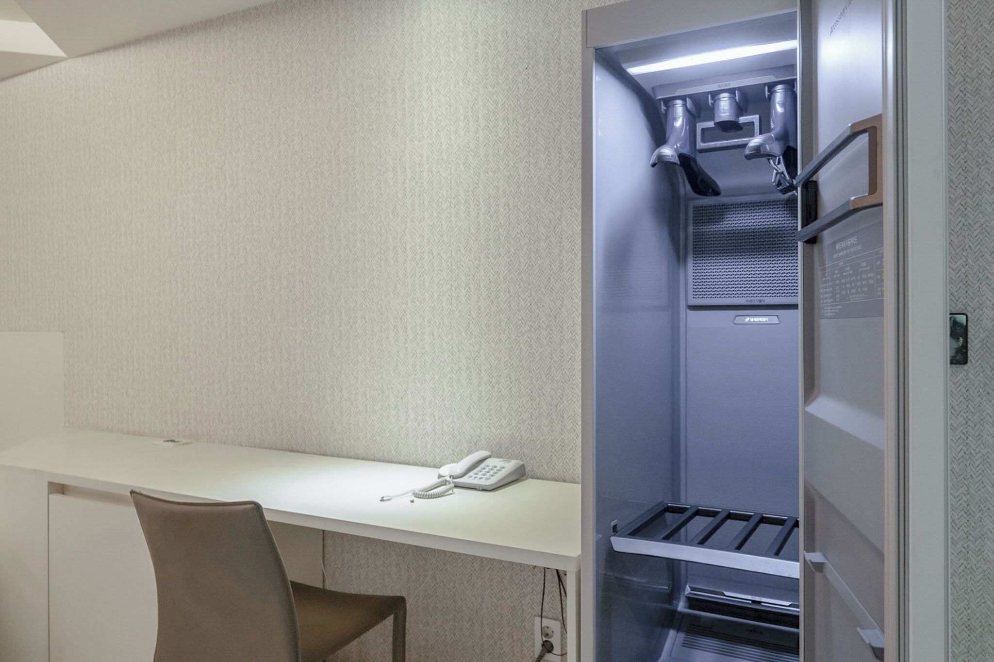 A hotel room with a white desk, a telephone, and a built-in wardrobe with a mirror and lighting.
