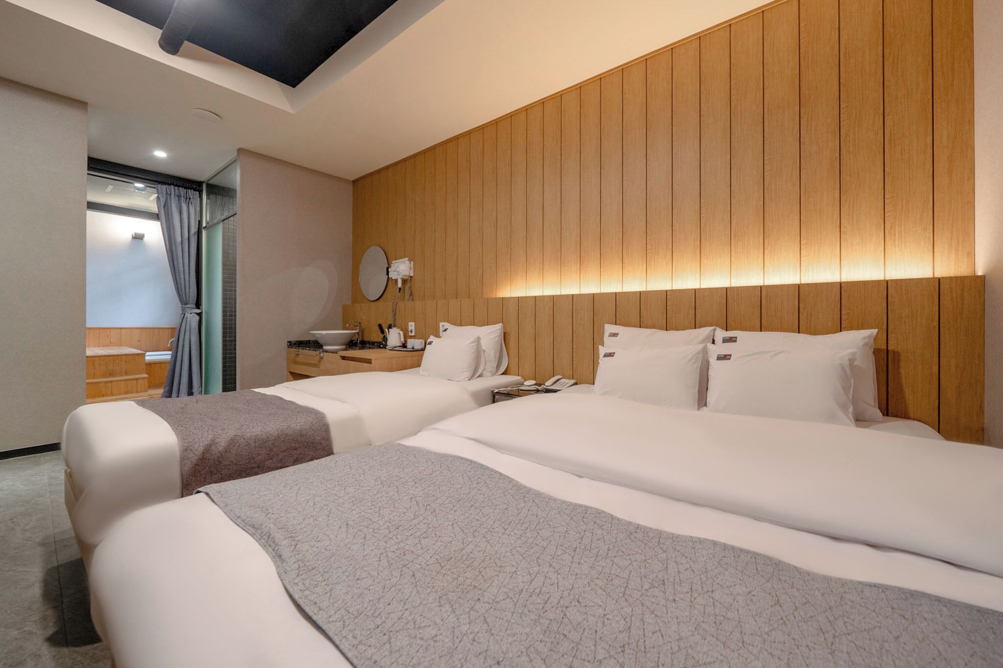 Une chambre d’hôtel avec deux lits, une tête de lit en bois, une table de chevet avec une lampe et une vue sur un espace sauna.