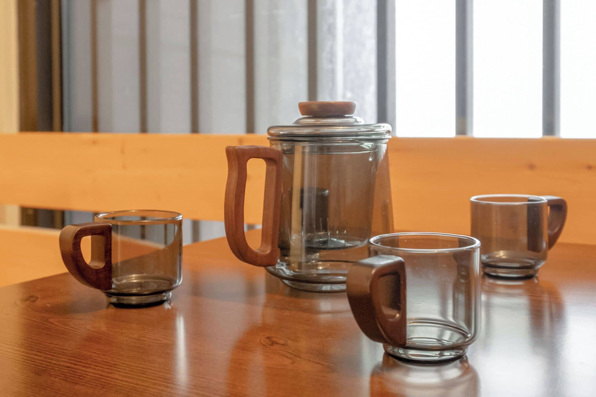 A wooden table with a glass coffee maker and four glass cups.
