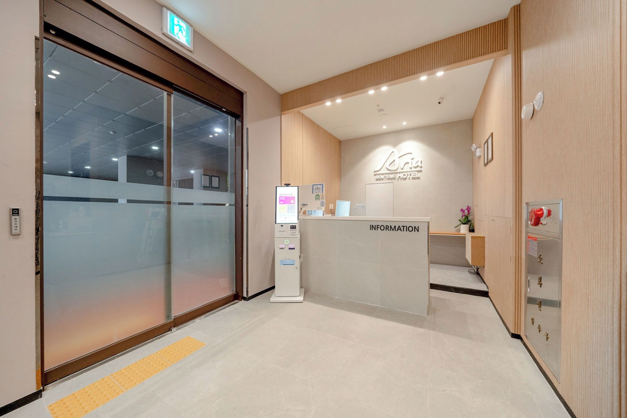 A hotel reception area with a modern design, including a reception desk, information kiosk, and a clear glass entrance.