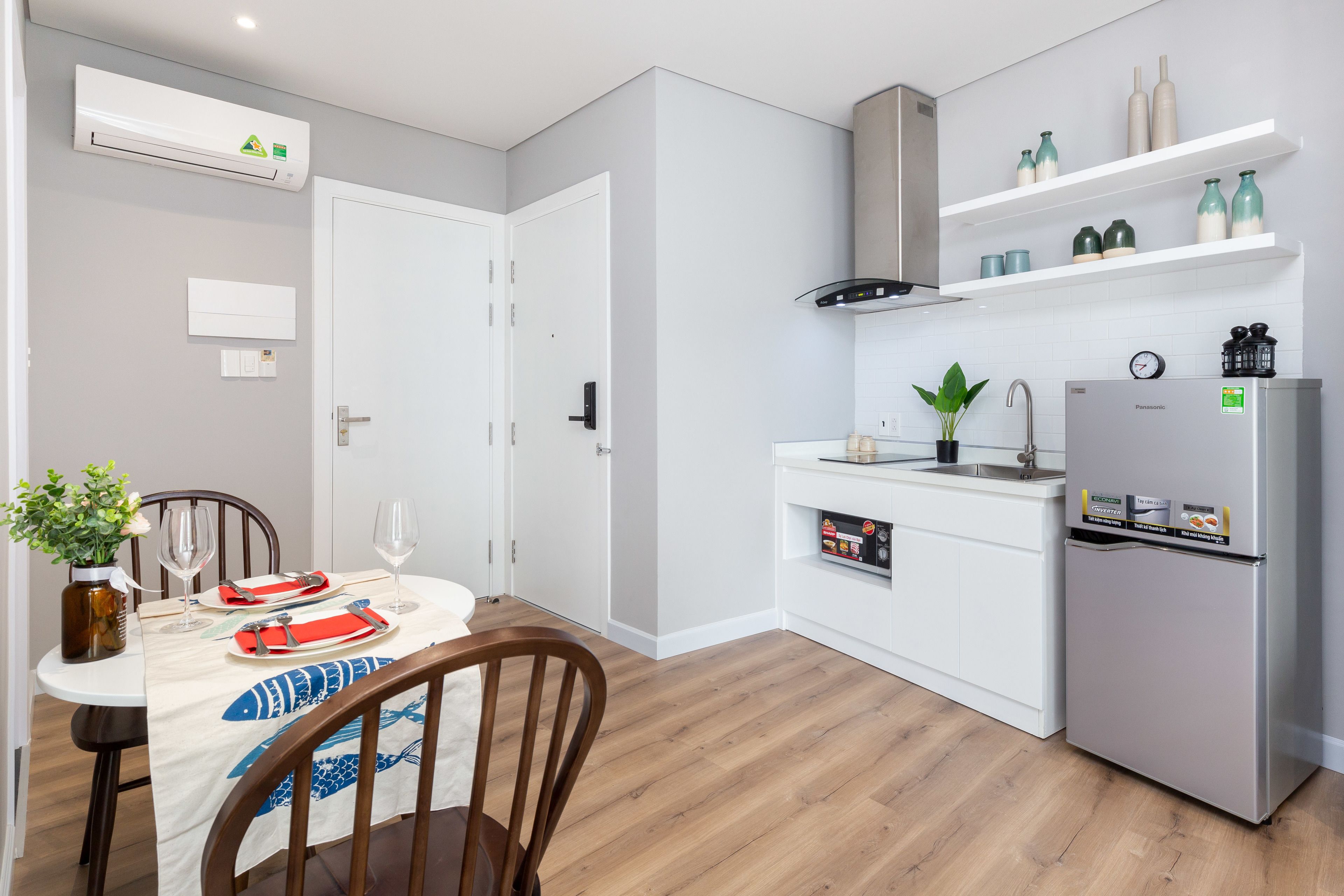 A modern kitchen with white cabinets, a stainless steel refrigerator, and a dining area with a table set for two.