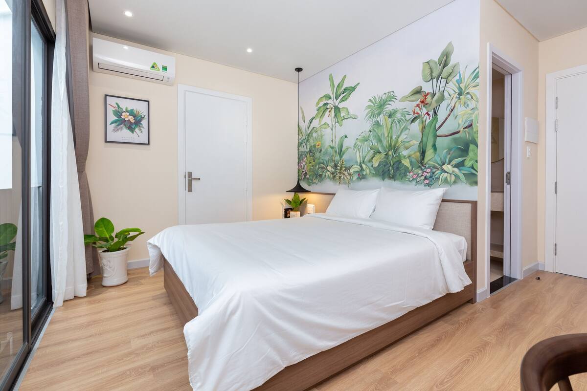 Une chambre à coucher avec un lit, une fresque représentant des plantes tropicales, une plante en pot et une fenêtre avec des rideaux.