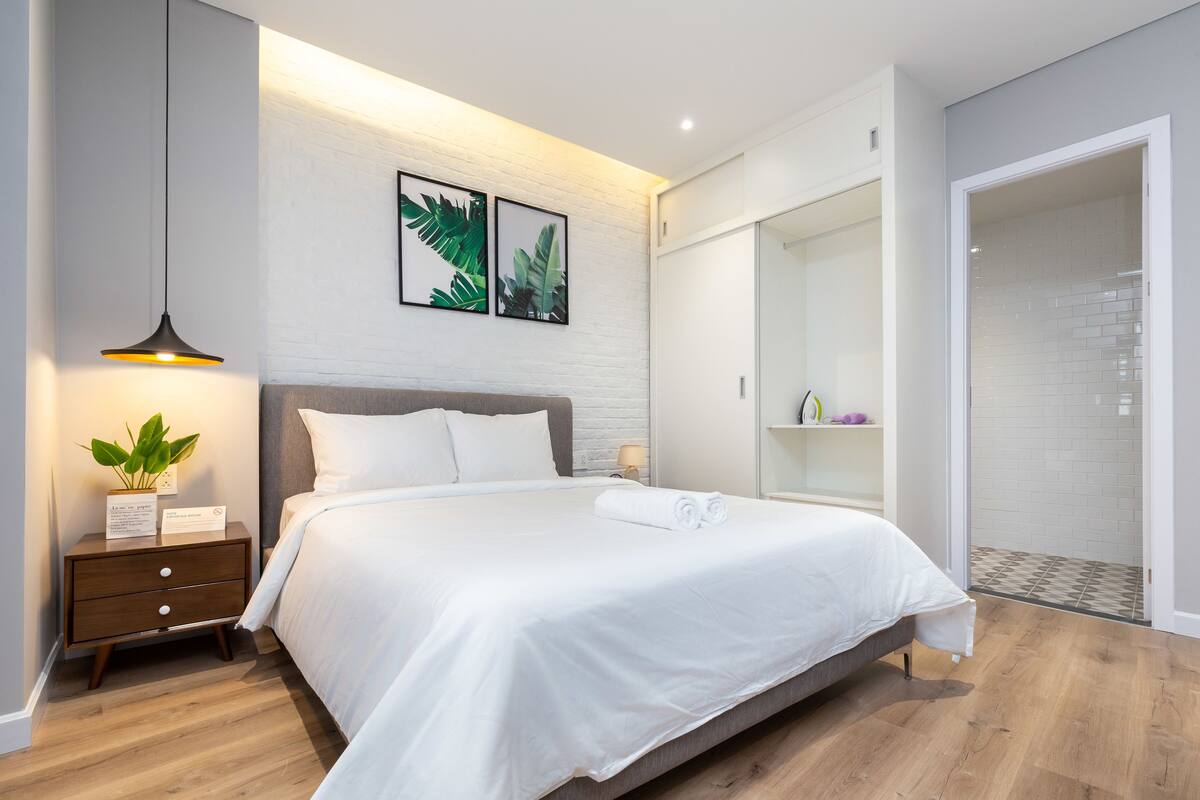 Une chambre à coucher moderne avec un grand lit, une table de chevet avec une lampe et une étagère fixée au mur.