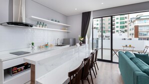 Una cocina moderna con encimera de mármol, estufa integrada y zona de comedor con sofá verde y sillas de madera.