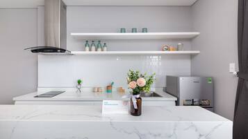 Eine moderne Küche mit weißen Arbeitsplatten, einer Edelstahl-Dunstabzugshaube und einem Kühlschrank. Darüber befinden sich Regale mit Flaschen und eine Vase mit Blumen. Ein Schild weist darauf hin, dass es sich um einen Nichtraucherraum handelt.