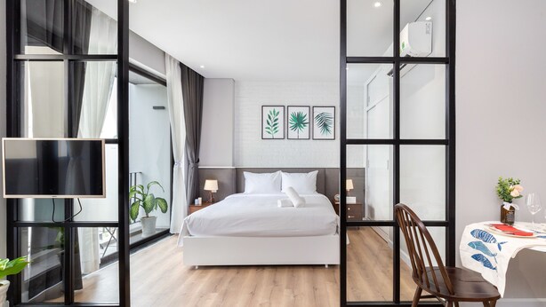 Una habitación de hotel moderna con una cama grande, un televisor, un área de comedor con una mesa y sillas, y un ventanal con cortinas.