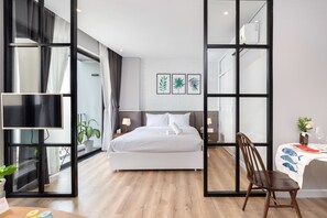 Une chambre d’hôtel moderne dotée d’un grand lit, d’une télévision, d’un coin repas avec une table et des chaises, et d’une grande fenêtre avec des rideaux.