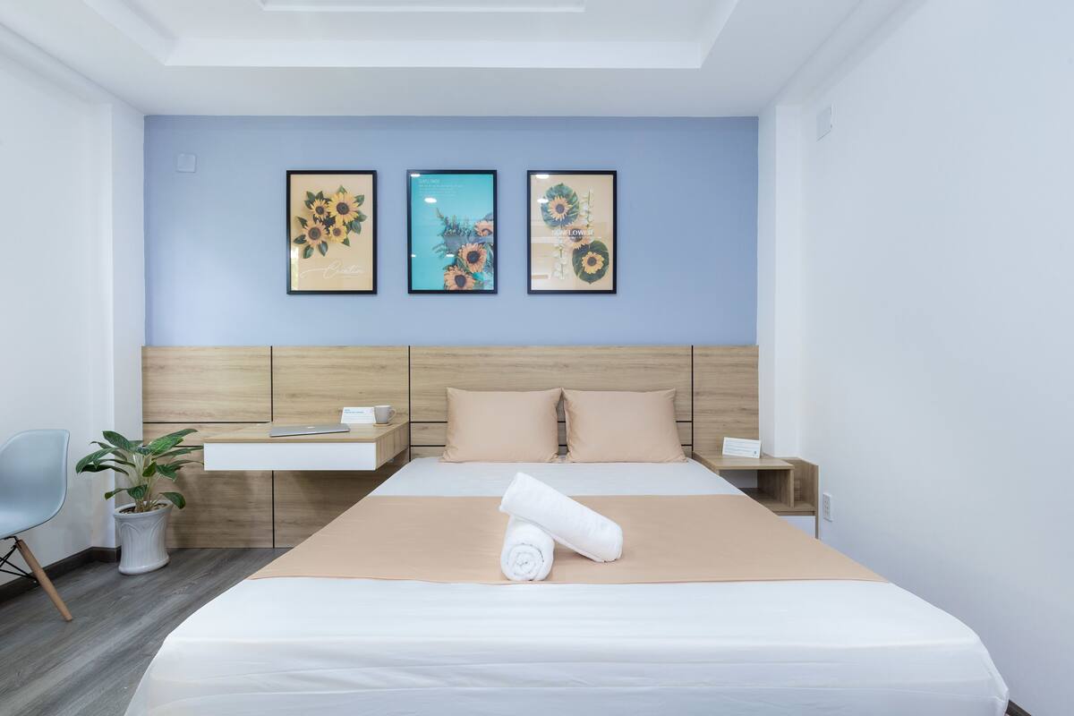 A hotel room with a bed, a nightstand, a chair, and a potted plant.