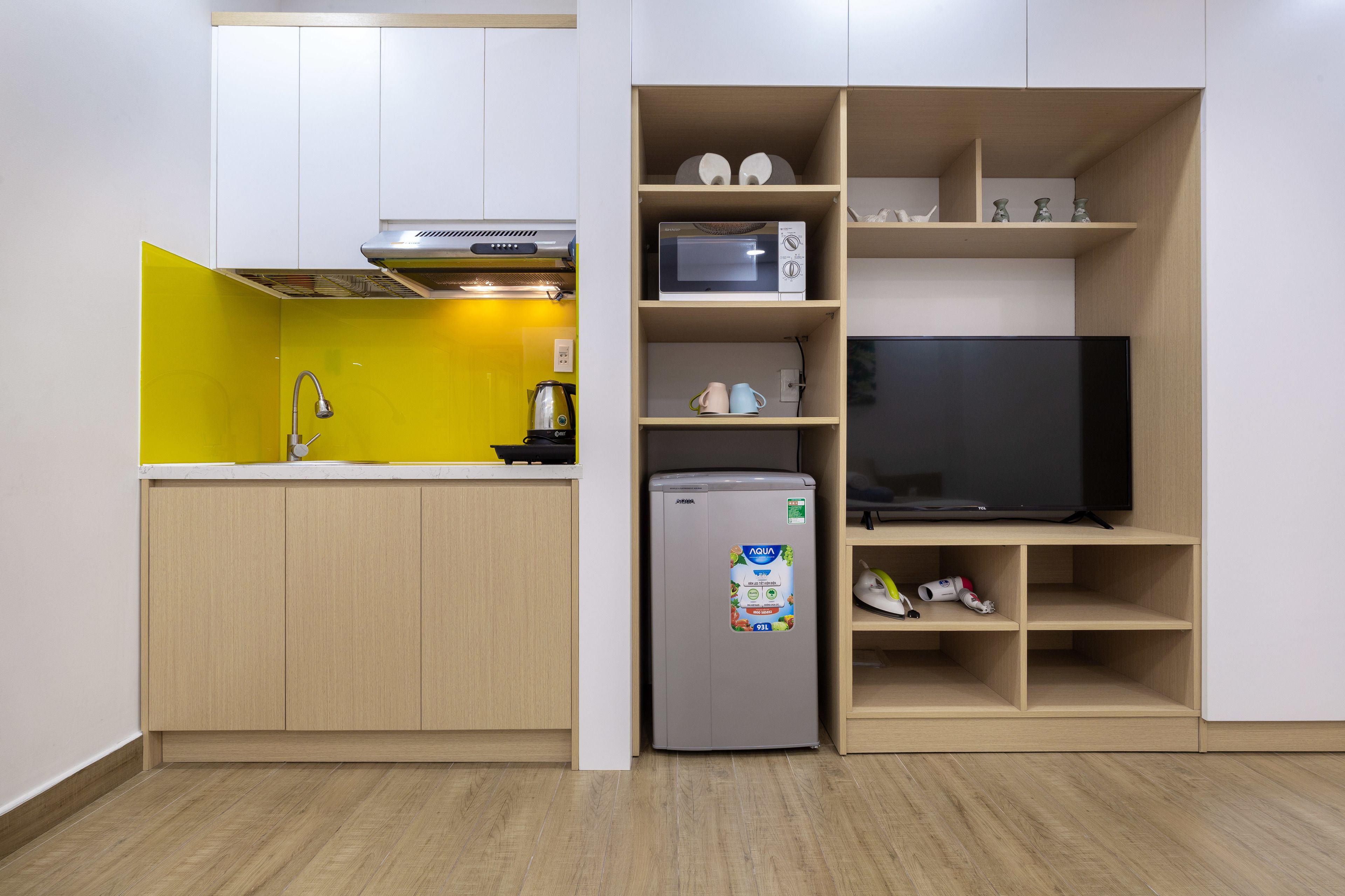 A compact kitchen with a microwave, refrigerator, and a flat-screen TV.