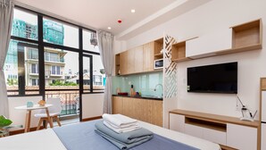 A modern hotel room with a large bed, a small kitchenette, a TV, and a balcony with a view of buildings. - Cozrum Homes Ly Chinh Thang (Ho Chi Minh City)