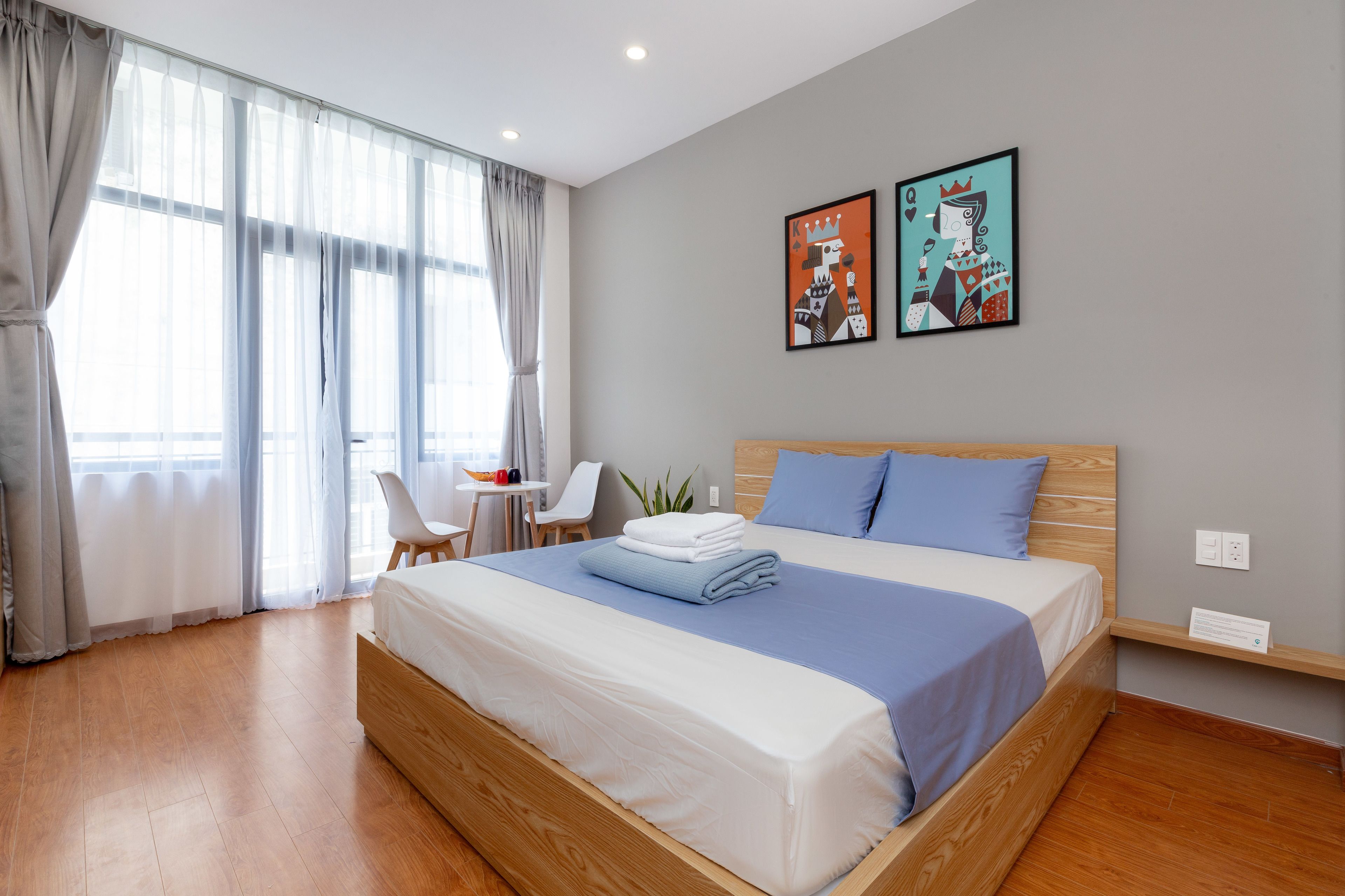 A modern hotel room with a large bed, a desk, and a chair. There are two framed artworks on the wall.