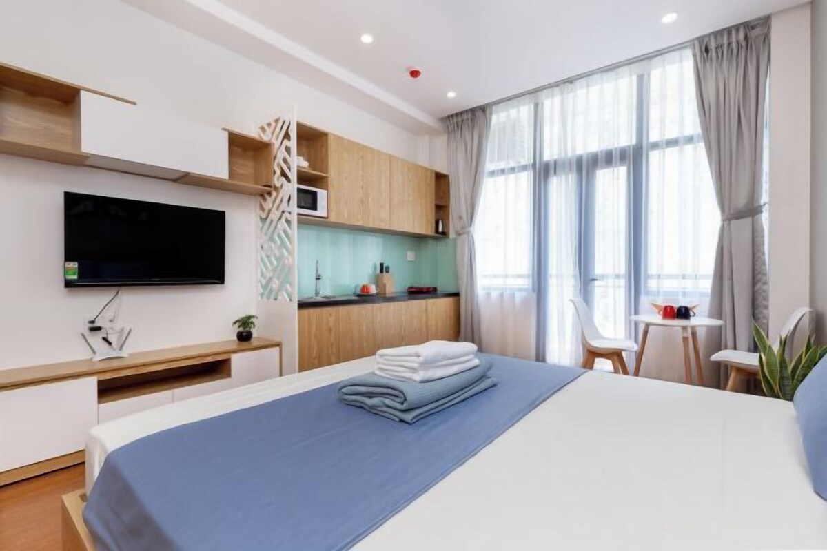 A modern hotel room with a bed, a TV, a kitchenette, and a dining area.