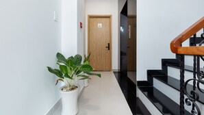 A hallway with a wooden door marked 302, a potted plant, and a staircase with black steps and a wooden handrail. - Cozrum Homes Ly Chinh Thang (Ho Chi Minh City)