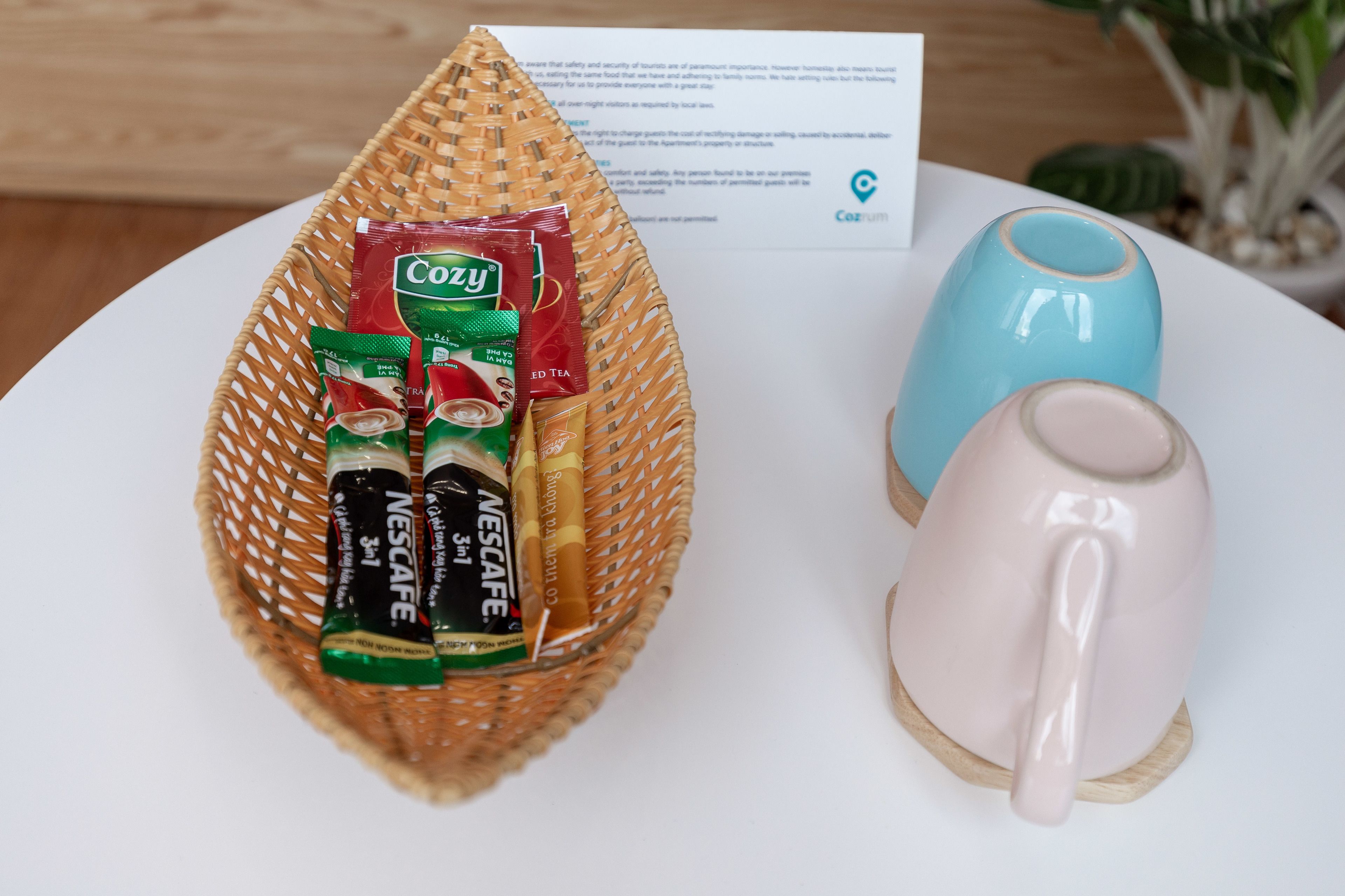 Een rieten mand met koffiepads en een blauwe mok op een witte tafel.