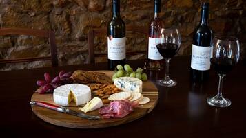A wooden board with cheese, crackers, and grapes, accompanied by wine bottles and glasses on a table.