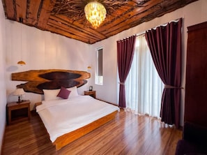 Une chambre à coucher avec un grand lit, une tête de lit en bois, un lustre et une fenêtre avec des rideaux.