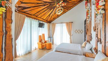 A hotel room with two beds, a wooden ceiling, curtains, a TV, and a floral decoration.
