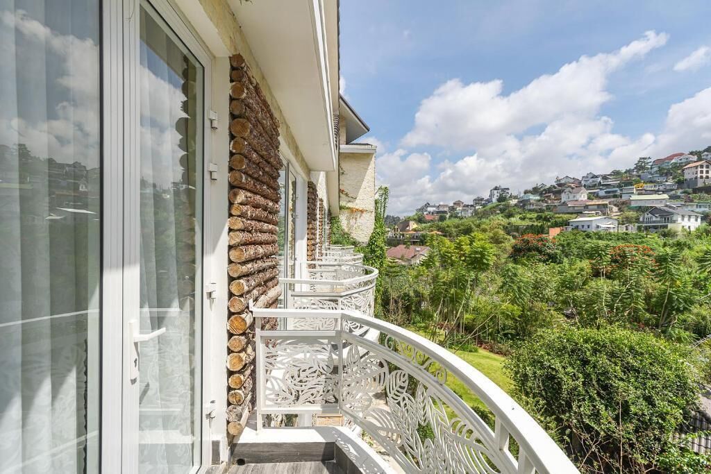 Un balcón con pared de piedra, barandilla blanca y vistas a un paisaje verde con casas.