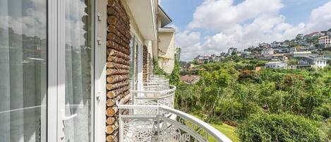 Un balcón con pared de piedra, barandilla blanca y vistas a un paisaje verde con casas.