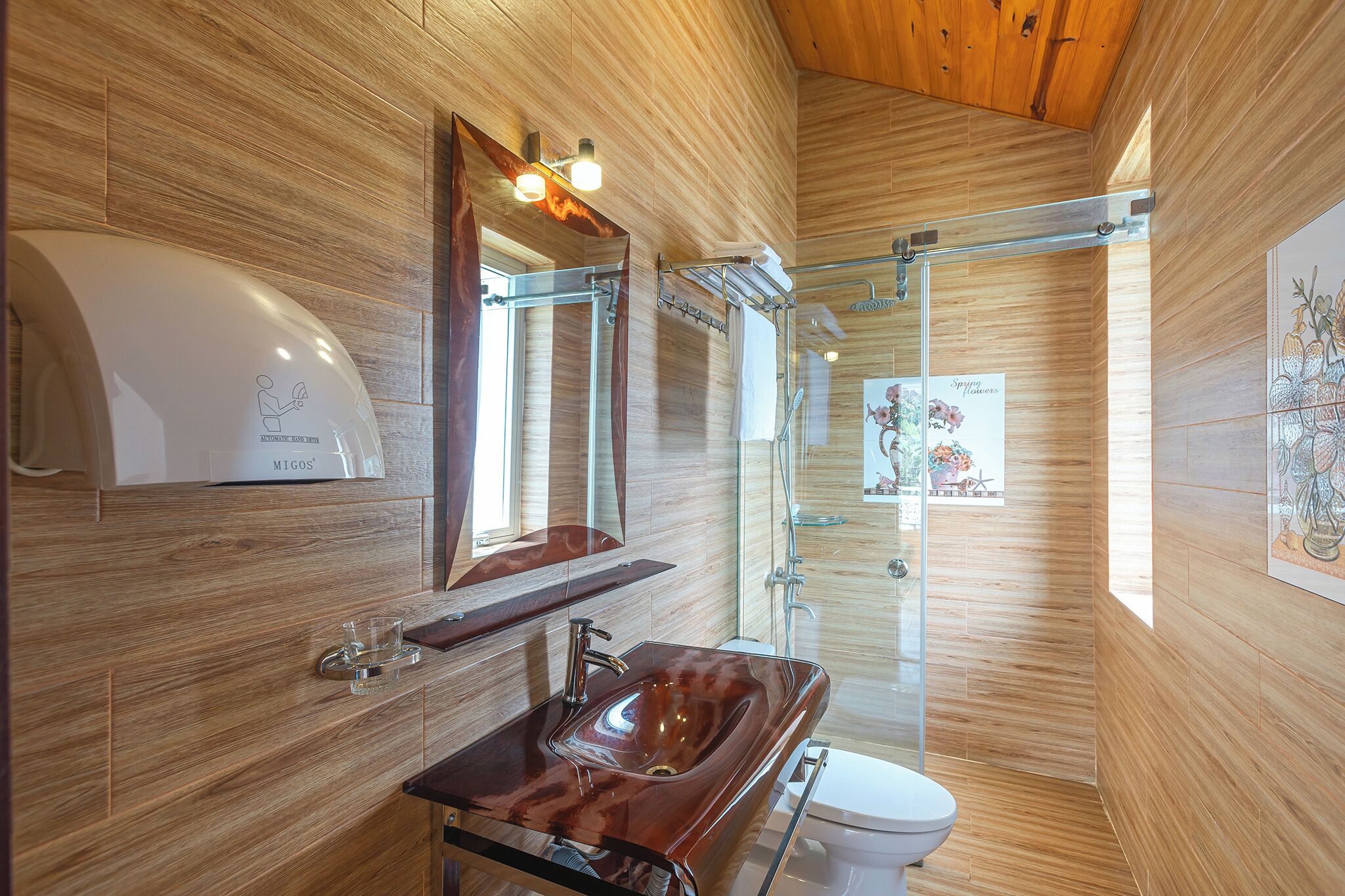 A modern bathroom with wooden walls, a glass shower enclosure, a wooden vanity with a sink, and a toilet.