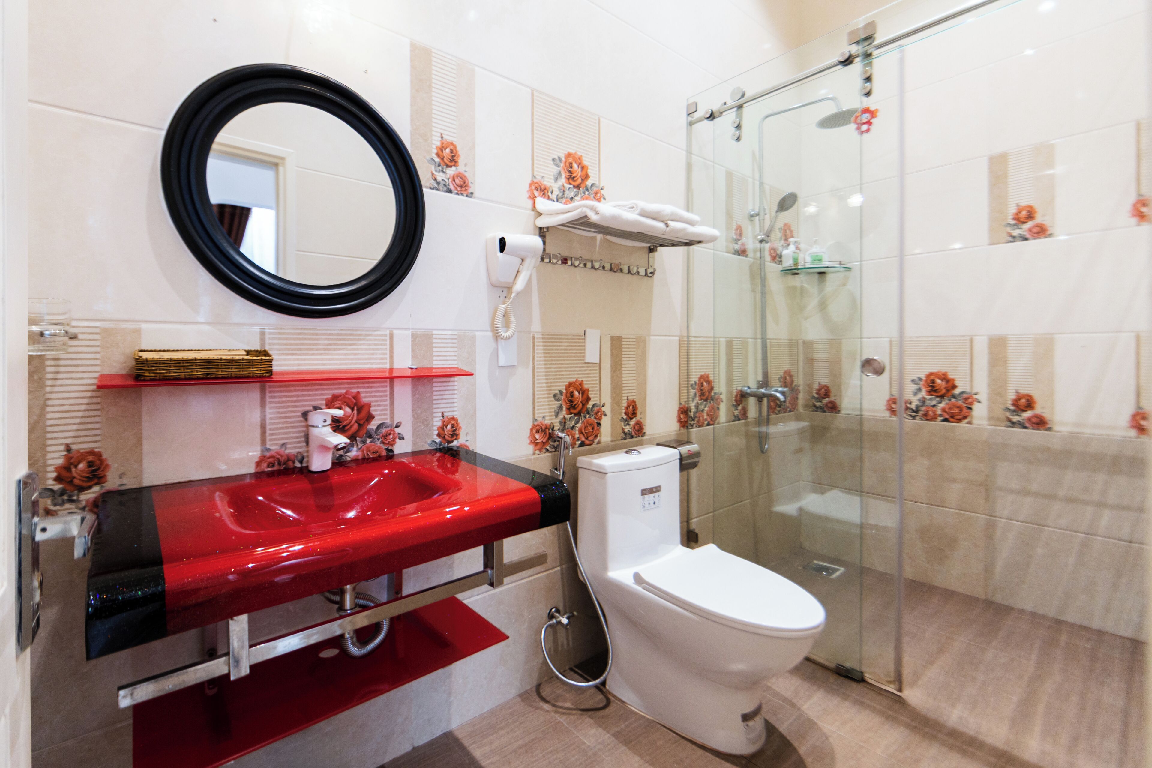 A bathroom with a red sink, a white toilet, a glass shower enclosure, and a mirror with a black frame.