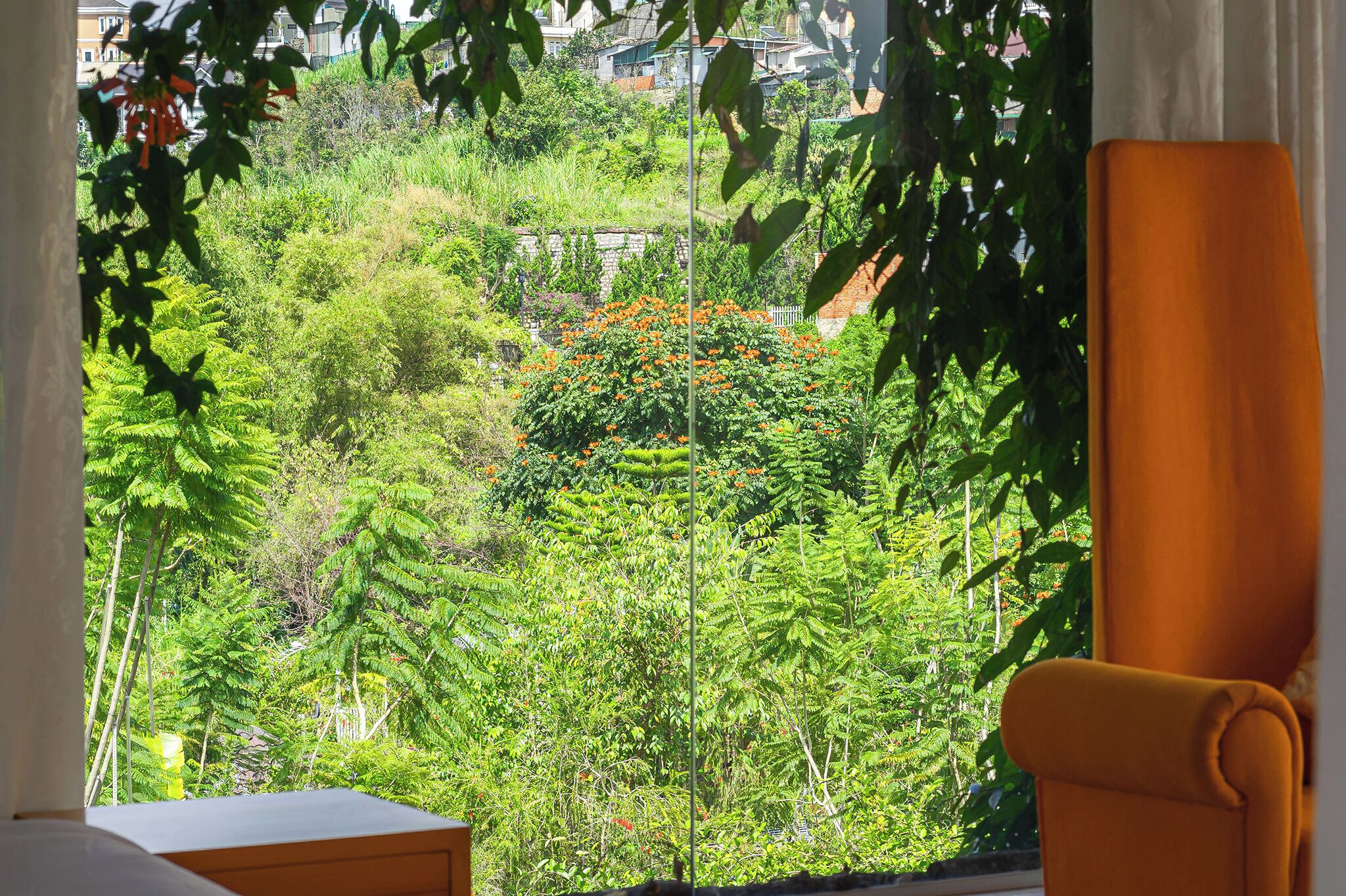 Une pièce donnant sur un jardin luxuriant, une fenêtre avec des rideaux et un fauteuil jaune.