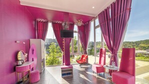 A room with a pink color scheme, large windows, a flat-screen TV, a red chair, and a small round table. - Mac Valley Dalat Hotel (Xuan Huong - Da Lat)