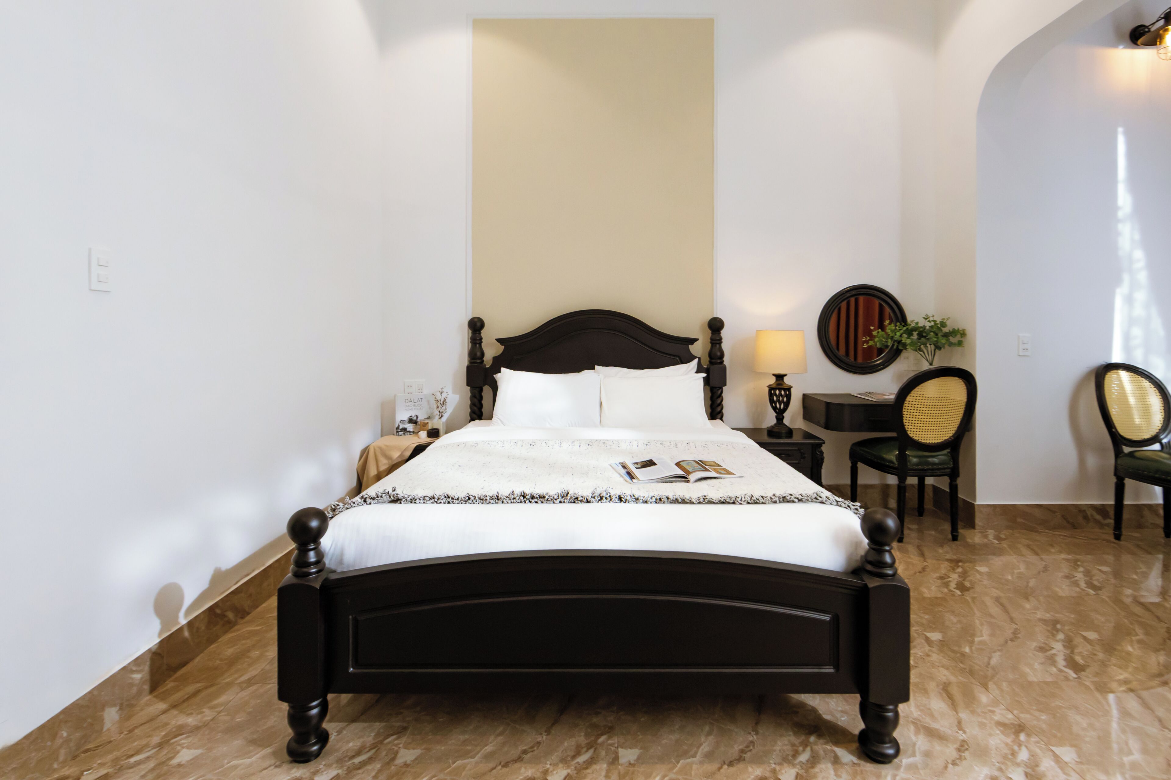 Ein ordentlich eingerichtetes Schlafzimmer mit Bett, Nachttisch, Lampe, Stuhl und einem wandmontierten Spiegel.