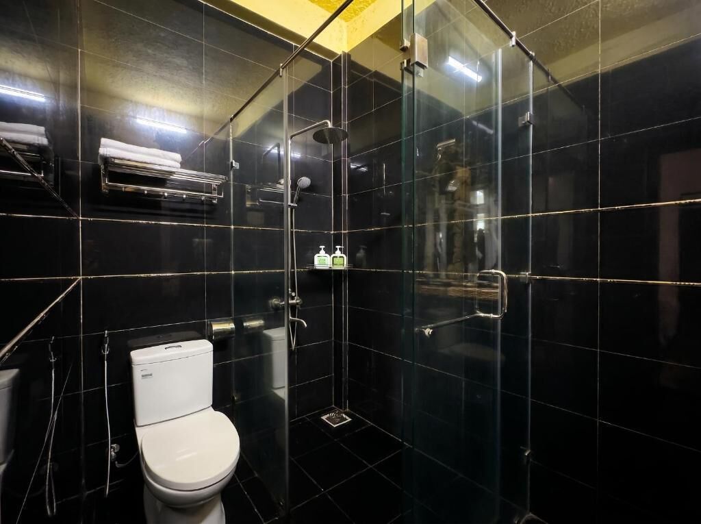 Une salle de bain comprenant des toilettes, une douche fermée par une paroi de verre et une étagère avec des articles de toilette.